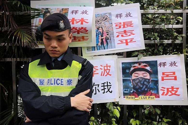 A Hong Kong police officer beside placards with photos of some of the missing booksellers from the Mighty Current publishing house, known for books critical of Beijing. In a TV broadcast on Sunday, four of them admitted to smuggling critical politica