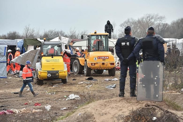 Policemen standing guard as agents and bulldozers dismantled shacks yesterday in the "Jungle" migrant camp in the French northern port city of Calais. An estimated 3,700 migrants are said to be in the camp, although humanitarian associations working 