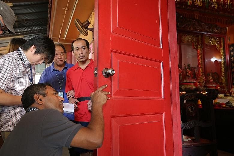 Murder suspect Loh (in red T-shirt) looking on as police investigators examine an area at the scene of the crime at Chin Long Kong Chinese Temple in Teck Whye Lane yesterday. Loh is accused of killing a man there.