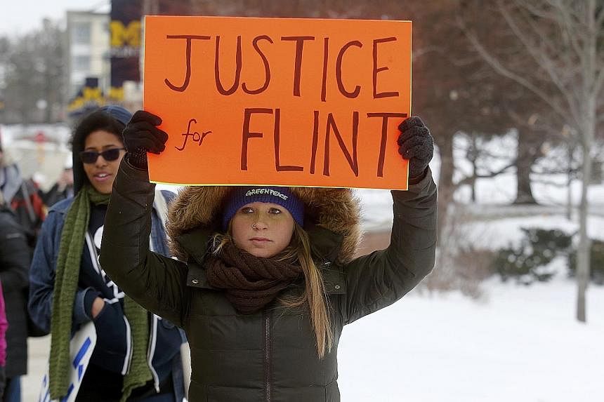 A volunteer distributing bottled water in Flint, Michigan. The city's water was tainted after its supply was switched under Republican governor Rick Snyder. Demonstrators (left) protesting against the crisis on Sunday.