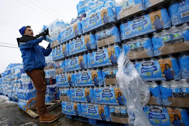 A volunteer distributing bottled water in Flint, Michigan. The city's water was tainted after its supply was switched under Republican governor Rick Snyder. Demonstrators (left) protesting against the crisis on Sunday.