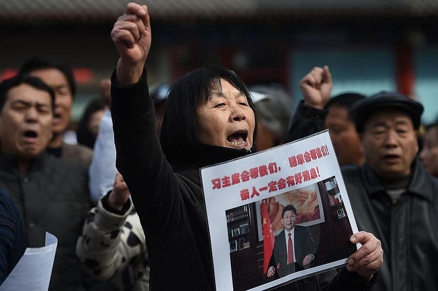 Ms Dai Shuqin holding a poster that reads "President Xi will help us. The nation will help us. Good news about our family is sure to come", as she took part in a protest outside Lama Temple in Beijing yesterday. Relatives of missing passengers on Fli