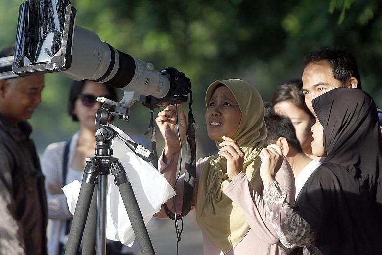 People crowding around a camera for a closer look at the solar eclipse in Jakarta yesterday, as it swept through 12 of Indonesia's 34 provinces before heading out towards the Pacific Ocean.