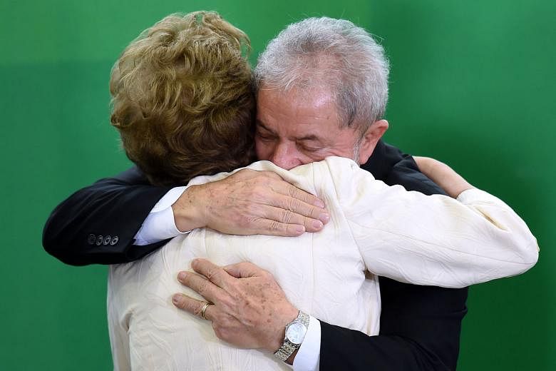 Mr Lula hugging Mrs Rousseff after she swore him into office on Thursday. He has been charged with graft, while she faces being impreached. 