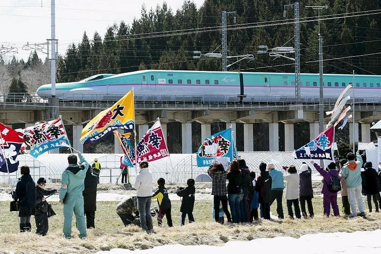 People waving flags as the first train of the new Hokkaido shinkansen, or bullet train, bound for Shin-Hakodate Hokuto Station from Tokyo, approached Kikonai Station in Kikouchi town on Japan's northern island of Hokkaido last Saturday. The long-awai