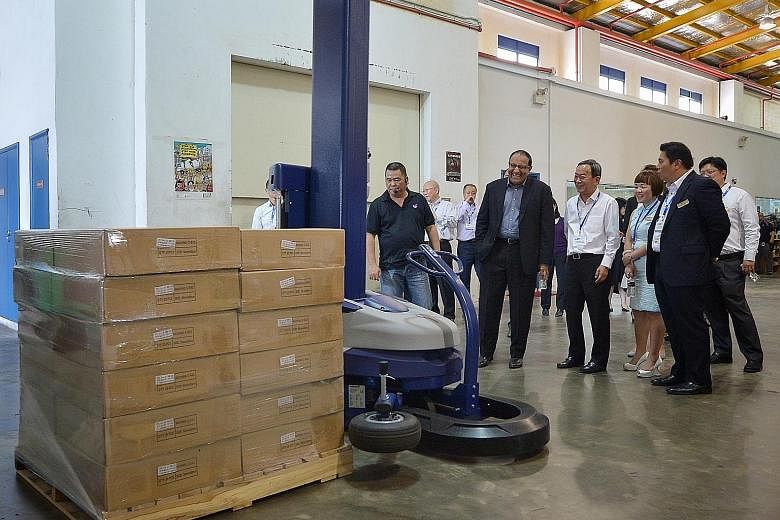Mr Iswaran (second from left) observing a demonstration by Goodrich Global logistics manager Steven Tan (far left) of a pallet wrapping robot. Mr Iswaran was accompanied by (from right) WAF's vice-chairman Neo Kah Kiat, its council member Audrey Chin