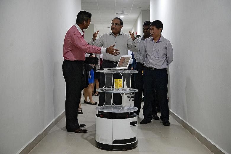 Mr Iswaran (centre) with Aitech Robotics and Automation industry robot engineer Sean Efrem Sabastian (far left) and business development manager Eric Lee at a demonstration of Aitech's food and beverage service robot's capabilities yesterday.