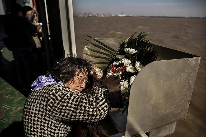 Madam Lin Hui Zhen, 76, clutches the bag carrying the ashes of her late husband Fu Yao Ming, 80, before placing it in a metal chute during a sea burial on a ferry in the East China Sea off Shanghai.