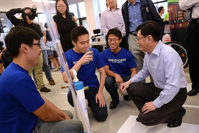 Mr Heng (at right) watching as Mr Lim Chong Tee, 24, chief marketing officer of start-up WateROAM, takes a sip of water from the company's Fieldtrate Plus, a water filter hand pump.