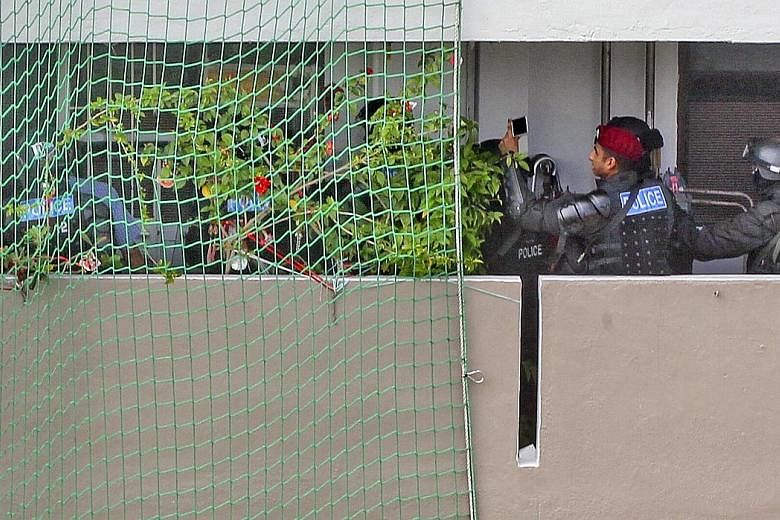 The suspected drug offender (left) being led away by police yesterday. The man trapped his mother in her bedroom of their flat (above) at Block 508, Ang Mo Kio Avenue 8, wielding a chopper and threatening to burn himself. Around 50 residents from the