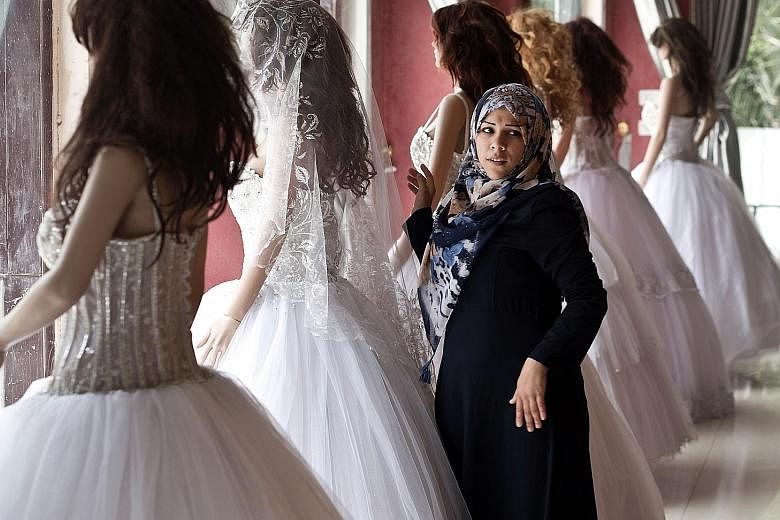 A Palestinian woman shopping for a wedding dress, a requirement for a lavish wedding on which young couples are expected to spend up to $27,000. It can take newlyweds several years to pay off the debt.