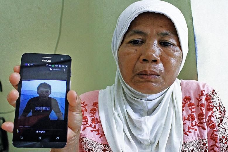 Ms Asmizar holding up a mobile phone on March 31 in Padang, West Sumatra province in Indonesia, showing a photograph of her son Wendy Rahadian - one of 10 members of a tugboat crew kidnapped by Islamic militants in the Philippines. The Indonesian sai