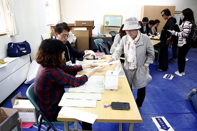 Voters receiving their ballot papers at a polling station in Seoul. Yesterday's voter turnout was about 58 per cent of the more 42.1 million eligible voters. Some analysts say a coalition government may emerge with the People's Party, led by Mr Ahn C