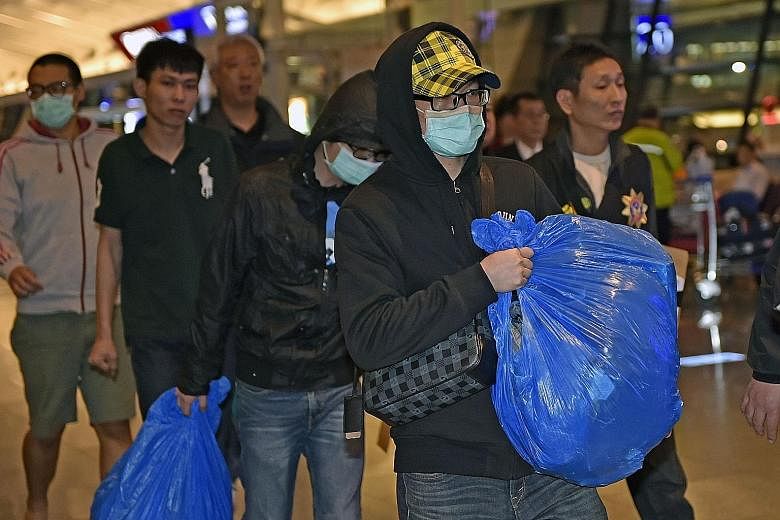 Taiwanese fraud suspects, (above, in masks) being escorted at Taoyuan Airport by Taiwanese police after being deported from Malaysia last Friday and (below, in hoods) being deported from Kenya to China as displayed on a monitor during a Taiwanese leg