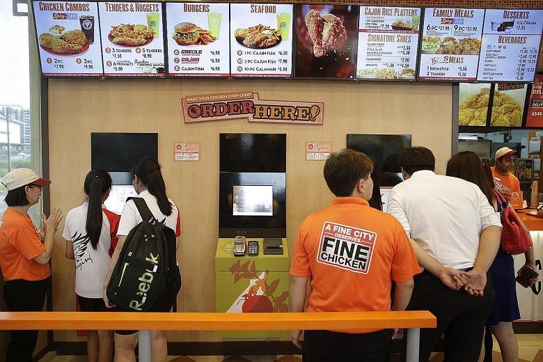 Customers placing their orders at self-ordering kiosks at Popeyes' Punggol East outlet. These kiosks have halved the time taken to place an order, leading to more efficient service and an increase in sales. The fried chicken chain intends to extend t
