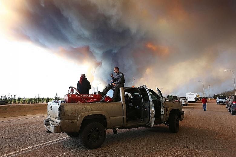A group trying to rescue animals from Fort McMurray waiting at a road block as smoke rises from a fire. Officials say the out-of-control inferno may keep burning for months without significant rainfall.