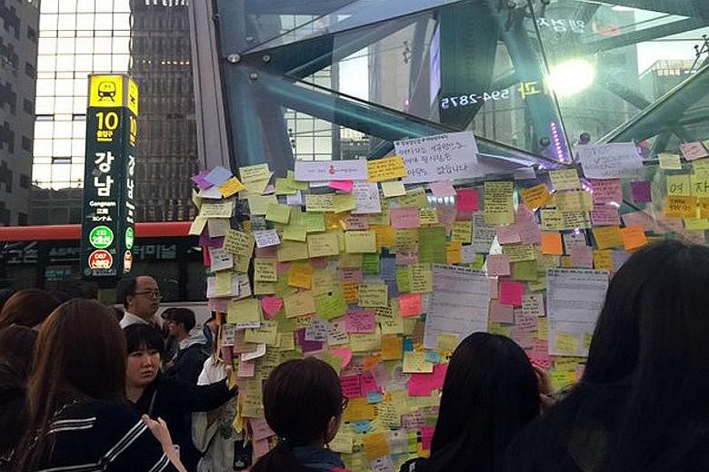 Passers-by looking at Post-it notes at the exit of Gangnam Station, written in memory of a woman stabbed nearby.