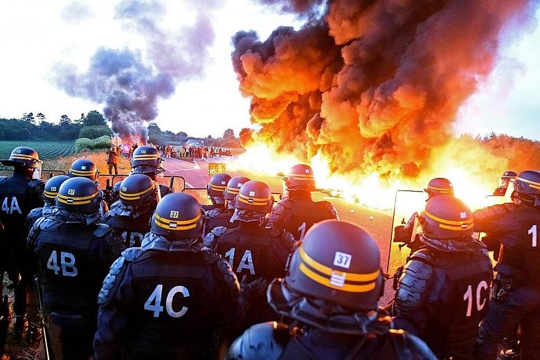 Riot police on guard behind a fire yesterday as refinery workers staged a blockade of the oil depot of Douchy-Les-Mines in northern France, to protest against the government's proposed labour reforms. Refinery workers stepped up strikes that threaten