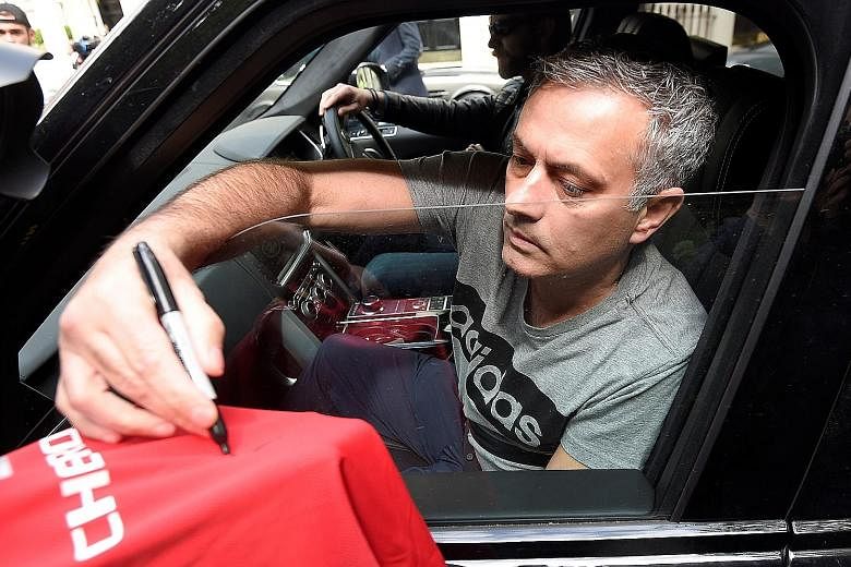 Jose Mourinho signs a Manchester United football shirt held out by a fan, while being driven from his home in London yesterday. "To become Manchester United manager is a special honour in the game," he said.