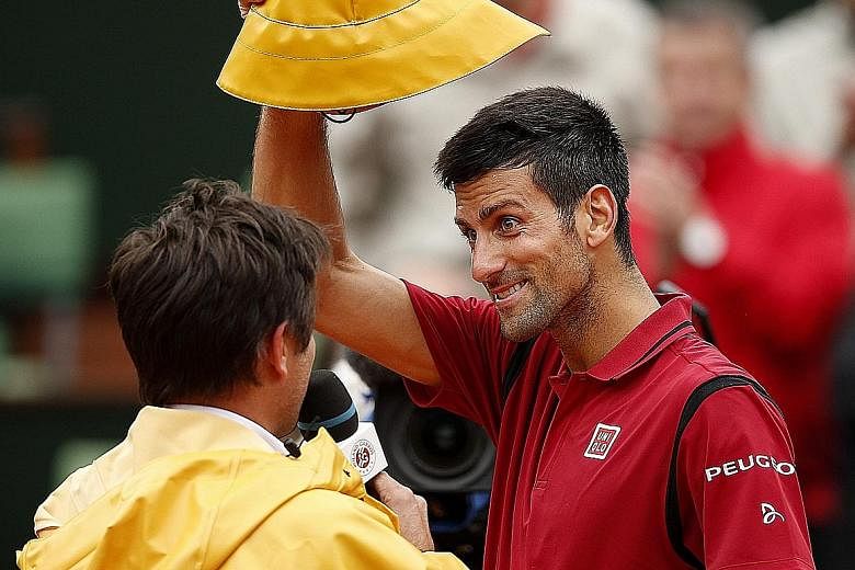 Novak Djokovic of Serbia borrows a rain hat from his interviewer, the former player Fabrice Santoro, after taking three days of play to defeat Roberto Bautista Agut of Spain in the round of 16 at the French Open. Turbulent weather in Paris has create