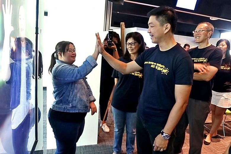 Minister Tan Chuan-Jin exchanging high fives with Ms Chen Wanyi, who has Down syndrome. Behind her is an interactive bus stop ad. If anyone high-fives her image in the ad, she would introduce herself and do a short dance. The bus stop ads are part of