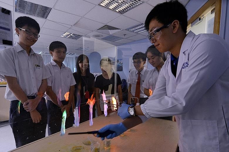 Students from Henderson Secondary School, and teachers Chian Yuan Lin and Yeo Ching Ying (third and fourth from left), observing how NUS student Tan Wei Zhi created various coloured flames at the Science Demo Lab in the university last month. Last ye
