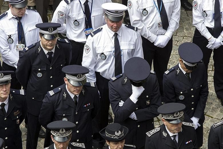 Police officers observing a minute of silence at a memorial ceremony held yesterday for an off-duty police officer and his wife who were fatally stabbed by an ISIS assailant.