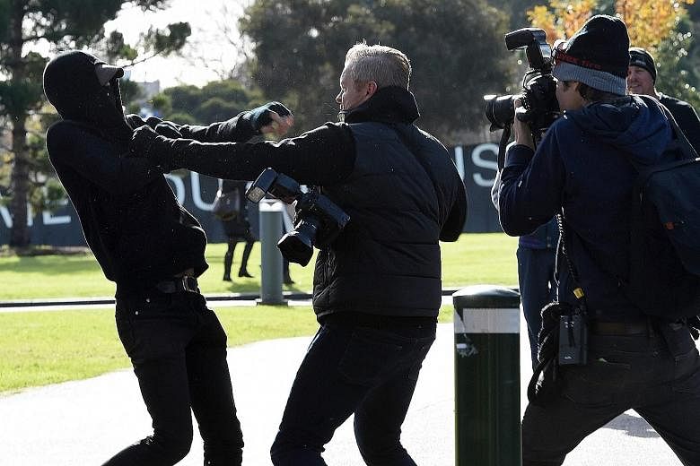 A demonstrator scuffling with a photographer during a rally outside Parliament House in Melbourne yesterday. Victoria state plans to impose stiffer penalties on mask-wearing protesters.
