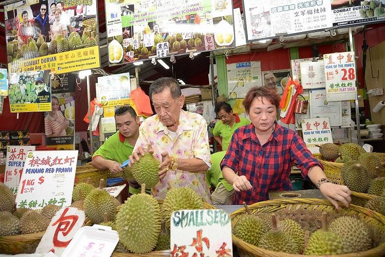 Madam Ang together with her father at their durian stall in Balestier Road. While prices have increased, she says customers will still buy the fruit if they "crave for it". Dry weather in Malaysia and Thailand has decreased durian harvests, and the p