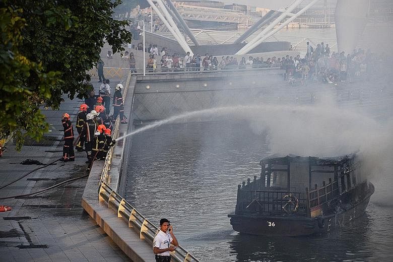 Massive plumes of smoke rising from the burning boat yesterday evening as people gathered on the walkway near the Esplanade. SCDF personnel (right) put out the fire using two water jets from the riverbank.