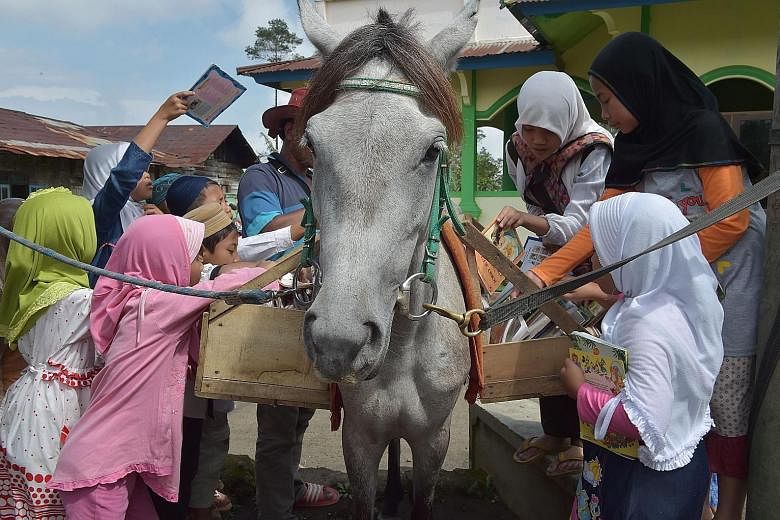 Indonesian children hunt for books from a mobile library on horseback as Mr Ridwan Sururi (partially hidden, with hat) compiles a book list for villagers in Serang, a quiet hamlet fringed by rice fields and a volcano on Indonesia's main island of Jav