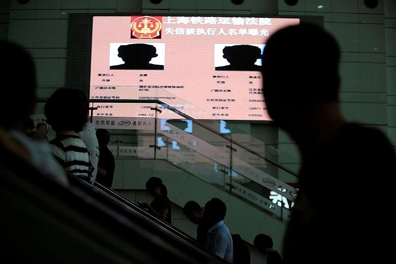 An electronic screen showing information of runaway debtors at a Shanghai railway station. As growth slows, borrowers are finding it harder to repay their loans, and Chinese courts have ramped up their use of shaming tactics.