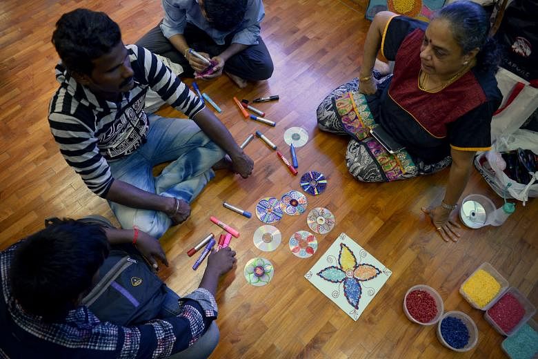 Some foreign workers learning to create Rangoli artwork from Ms Vijaya Mohan (right). Rangoli, a form of Indian floor art, is created with household items like pasta, rice grains and recycled utensils.