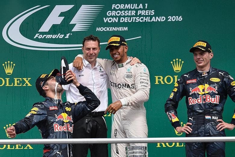 German Grand Prix winner Lewis Hamilton (white overalls) watches on as Daniel Ricciardo drinks champagne out of a shoe beside his Red Bull team-mate Max Verstappen.