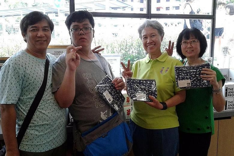 Sheng Jie with his parents - taxi driver See Toh and manager Wendy Chua, 52 - and Mrs Lee at the Enabling Village in Lengkok Bahru with the dinosaur purses he designed.