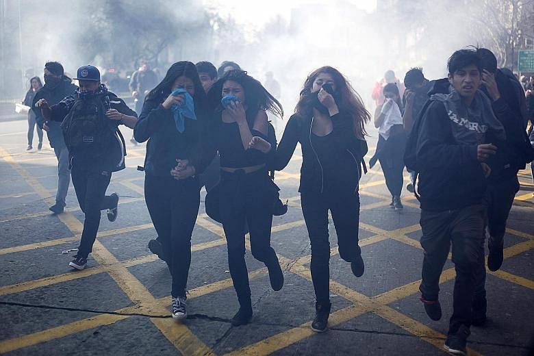 Chilean student protesters covering their faces after police fired tear gas during a clash in Santiago de Chile on Thursday. Thousands of students took to the streets in the capital and other cities in Chile to denounce a proposed education overhaul 