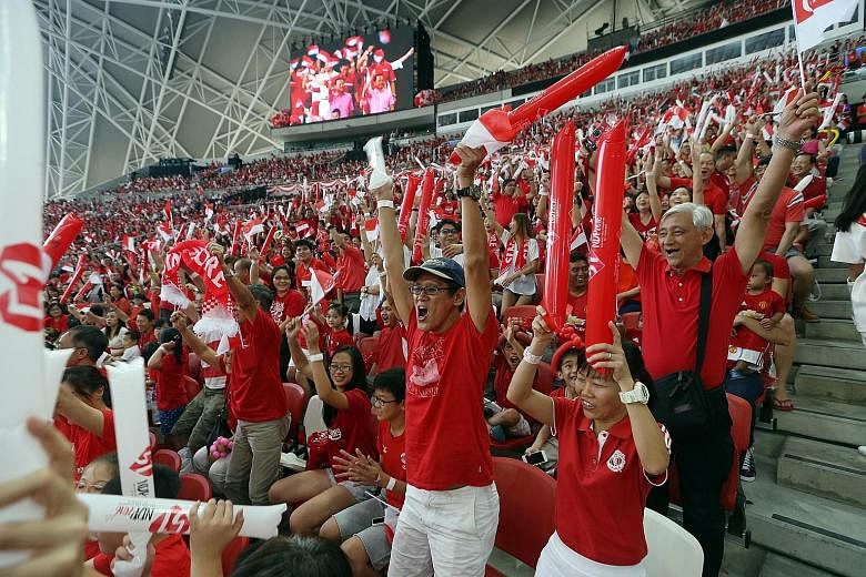 Above: Parade-goers get on their feet and roar as the Kallang Wave sweeps across the National Stadium - the site where the tradition was born. Many whip out the Singapore scarf for the ritual which lasts a good three to four minutes. Left: Participan