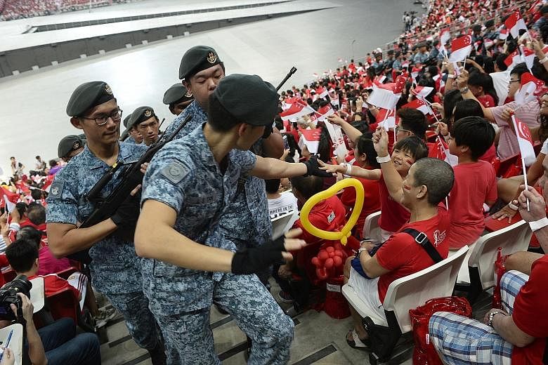 Above: Parade-goers get on their feet and roar as the Kallang Wave sweeps across the National Stadium - the site where the tradition was born. Many whip out the Singapore scarf for the ritual which lasts a good three to four minutes. Left: Participan