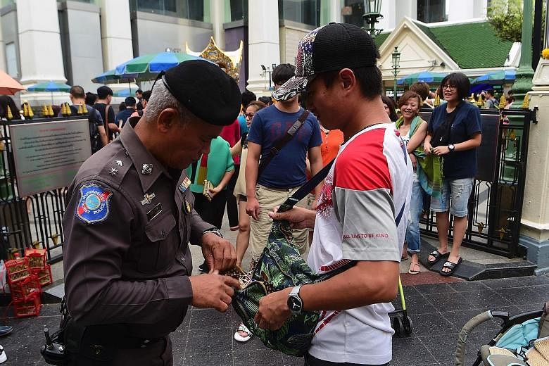 A Thai policeman searching a visitor's bag yesterday at the Erawan Shrine in Bangkok as the authorities increase security following a string of bomb attacks in Phuket and other southern provinces last week. A mobile phone used to trigger an explosion