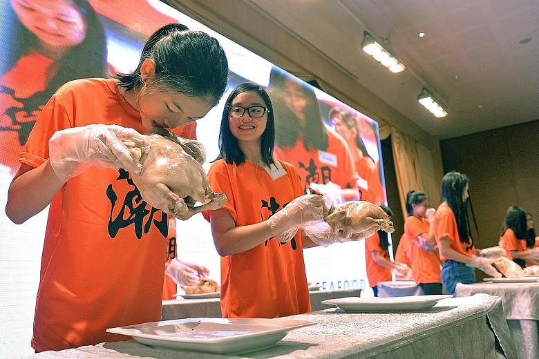 Student Geena Ang having a go at a rooster's head, alongside her schoolmate Andrea Chua, while taking part in the ancient Teochew coming-of-age ritual known as Cu Huay Hng at Chui Huay Lim Club yesterday.