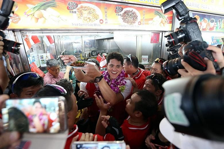 Schooling with a plate of his favourite black chye tow kueh from Bee Bee Carrot Cake at Marine Terrace Market, his first pit stop during his victory parade yesterday. Cheering fans not only packed the pit stops, but lined the bus route to show their 