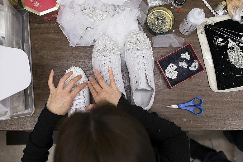 An employee at Kleinfeld Bridal in New York applying decorative elements to running shoes (left) for a bride to wear under her wedding gown.