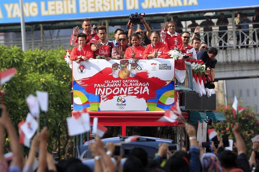 Above: Members of the Indonesian Olympic badminton team, including gold medallists Liliyana Natsir (left) and Tontowi Ahmad (third from left) wave from a bus while being paraded down a street in Jakarta yesterday.