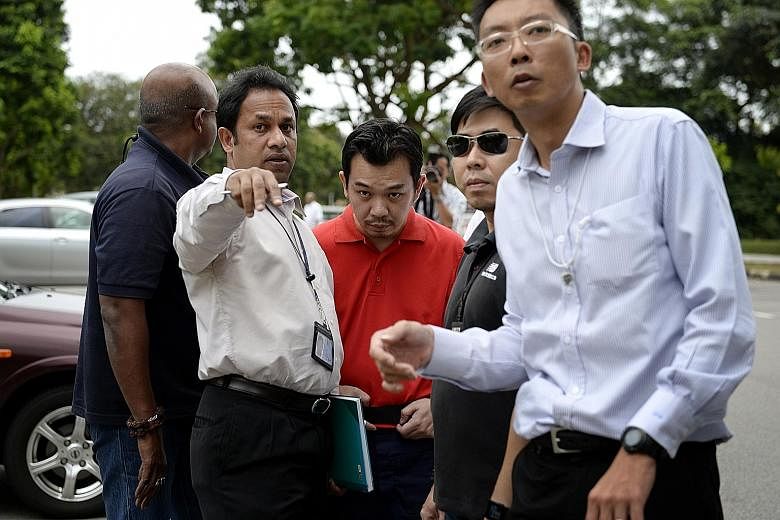 Investigators taking Lee (in red) back to Sembawang Park in 2014, where he led them to the bag which contained the ransom money. He had thrown it into the bushes.