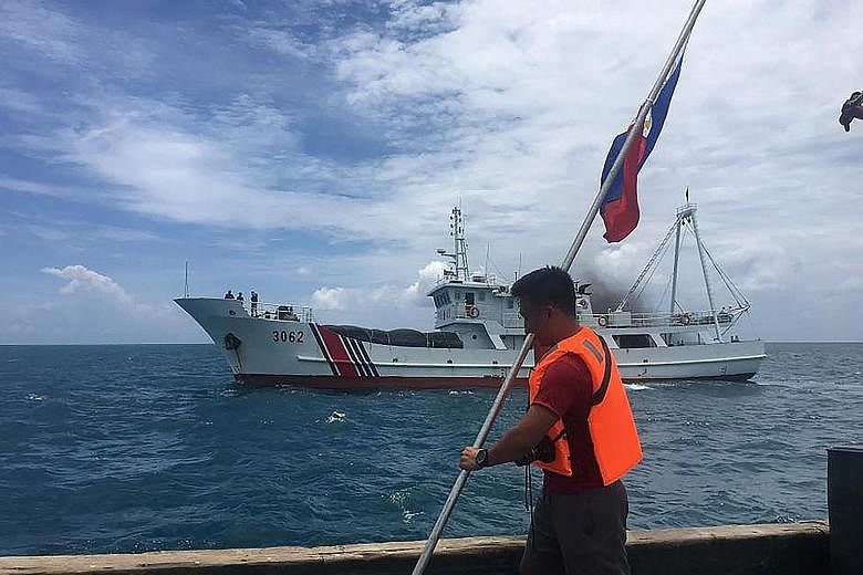 A Philippine activist holding his country's flag while a Chinese coast guard vessel sails near his ship at the Scarborough Shoal, just 220km west of the main Philippine island of Luzon.