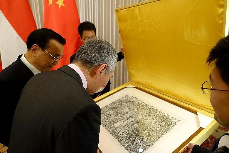 Prime Minister Lee Hsien Loong looking at a print of Singapore scenes presented to him by his Chinese counterpart Li Keqiang. Mr Lee received the 36cm by 49cm artwork by Chinese artist Zhang Minjie - featuring HDB flats, the Merlion, Marina Bay Sands