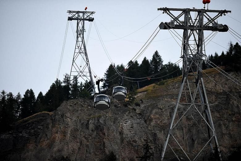 Above: One of the tourists being lowered to the ground. Seventy-seven of the stranded passengers had been rescued on Thursday, most by helicopters. Right: Two of the dangling cable cars. The incident was caused by cables becoming crossed for unknown 