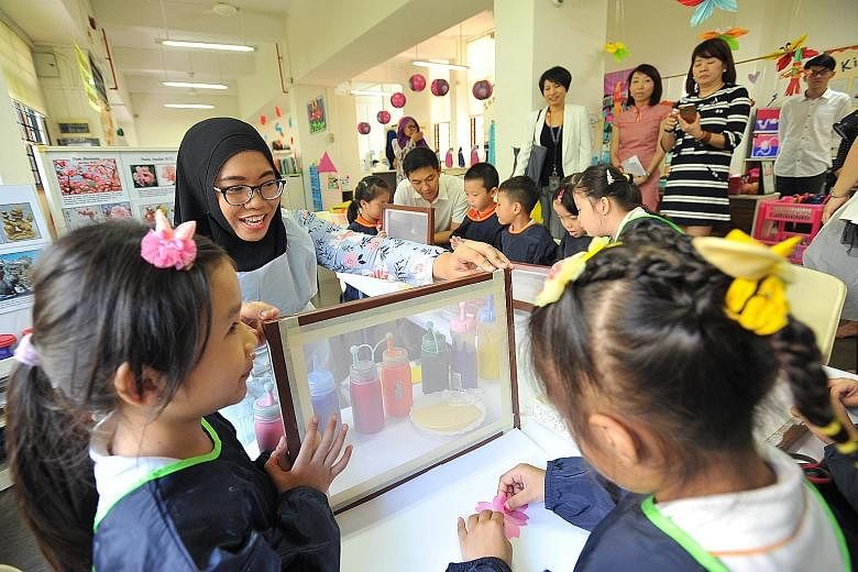 English teacher Nurulhuda Rahmat doing silkscreen printing with her pupils during a visit by Social and Family Development Minister Tan Chuan-Jin (in the background) at My First Skool in Haig Road yesterday. The 29-year-old is in the first batch of t