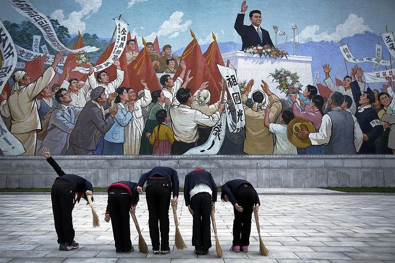 North Korean schoolgirls holding brooms pay their respects to late North Korean leader Kim Il Sung, seen in a mural, before sweeping the surrounding area on Dec 1 last year in Pyongyang.