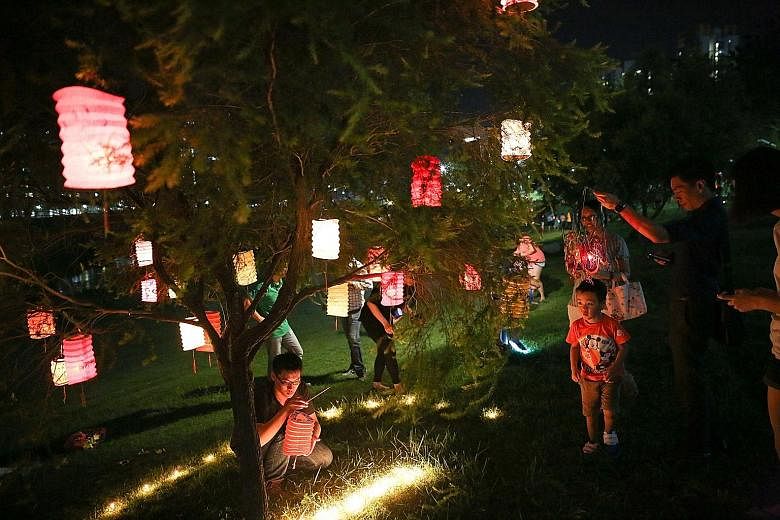 Mr Beh Kien Tai (crouching), 28, a sales coordinator at an air-conditioning company, hanging lanterns on a tree with a group of colleagues at the Bishan-Ang Mo Kio Park last night and attracting onlookers during yesterday's celebration of the Mid-Aut